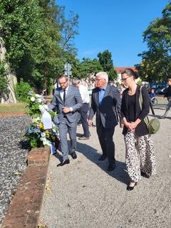 Drei Menschen tragen einen Kranz zur Gedenkstätte.