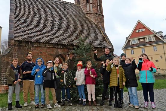 Die Künstler mit Bauer Matthias Lau mit dem Weihnachtsbaum vor der Kapelle