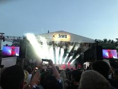 Bühne mit starker Beleuchtung am Abend, im Vordergrund jubelnde Menschen