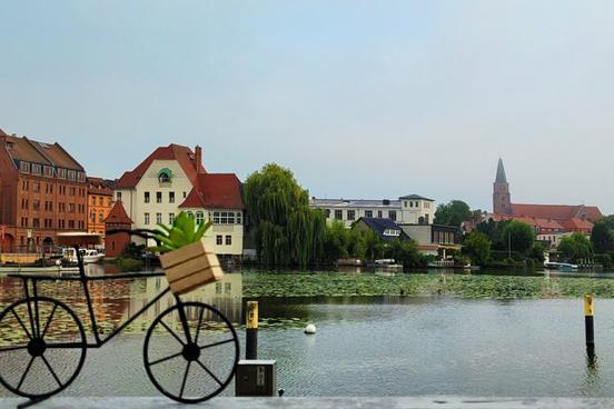 Miniatur-Fahrrad im Vordergrund, im Hintergrund Wasser und Häuserfronten am Wasser sowie der Dom zu Brandenburg
