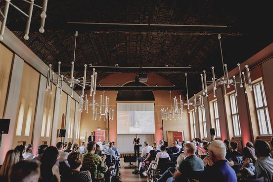 Blick in den Saal mit Teilnehmern auf Stühlen.