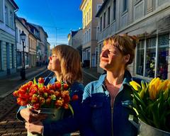 Zwei Frauen genießen die Sonnenstrahlen und halten Tulpen in großen Töpfen in den Händen.