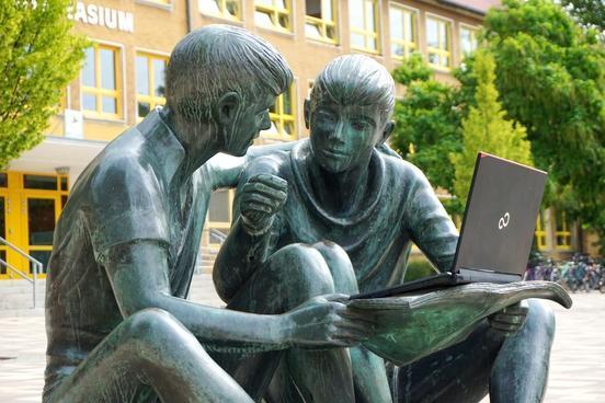 Statue von 2 Schülern vor dem Bertolt-Brecht-Gymnasium; die Schüler halten ein Buch in der Hand, aber darauf steht ein Laptop