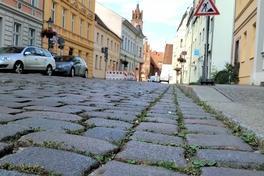 Im Vordergrund Pflastersteine der Straße, im Hintergrund Autos, Baustellenschild und Altstädtisches Rathaus