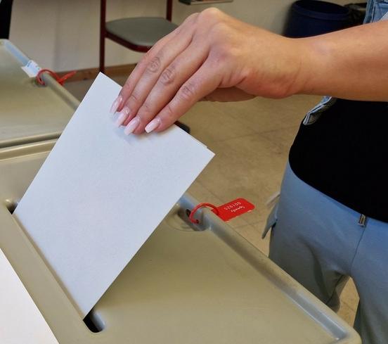 Eine Person steckt Wahlzettel in die Wahlurne