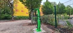grüne Säule mit Werkzeug und Hängevorrichtung vor der gelben Wand der Schule am Krugpark