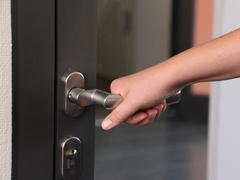 Eine Hand greift eine silberne Türklinke.