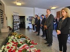 Menschen vor Kränzen an einer Erinnerungsstätte.