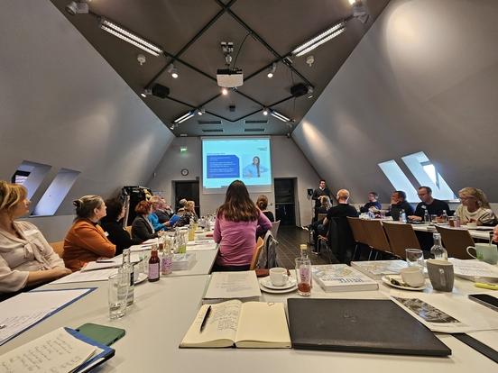 Menschen sitzen in einem Konferenzraum und schauen sich eine Präsentation an