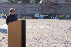 Oberbürgermeisterin steht am Pult, im Hintergrund eine Wand mit niedergelegten Kränzen