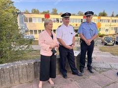 3 Personen stehen auf einem Gehweg nahe einer Kita und einer Grundschule